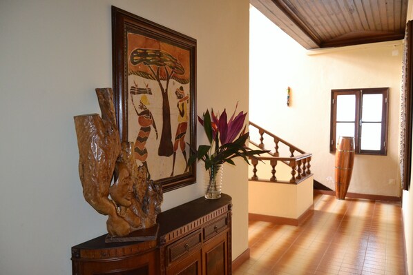 A hallway with a wooden staircase, a framed painting, and a vase with flowers.
