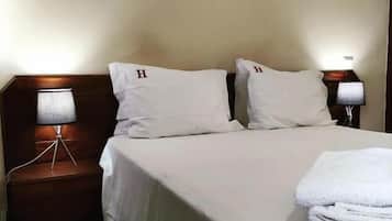 A hotel room with a bed, two pillows, a headboard, a nightstand with a lamp, and a wall-mounted decorative item.
