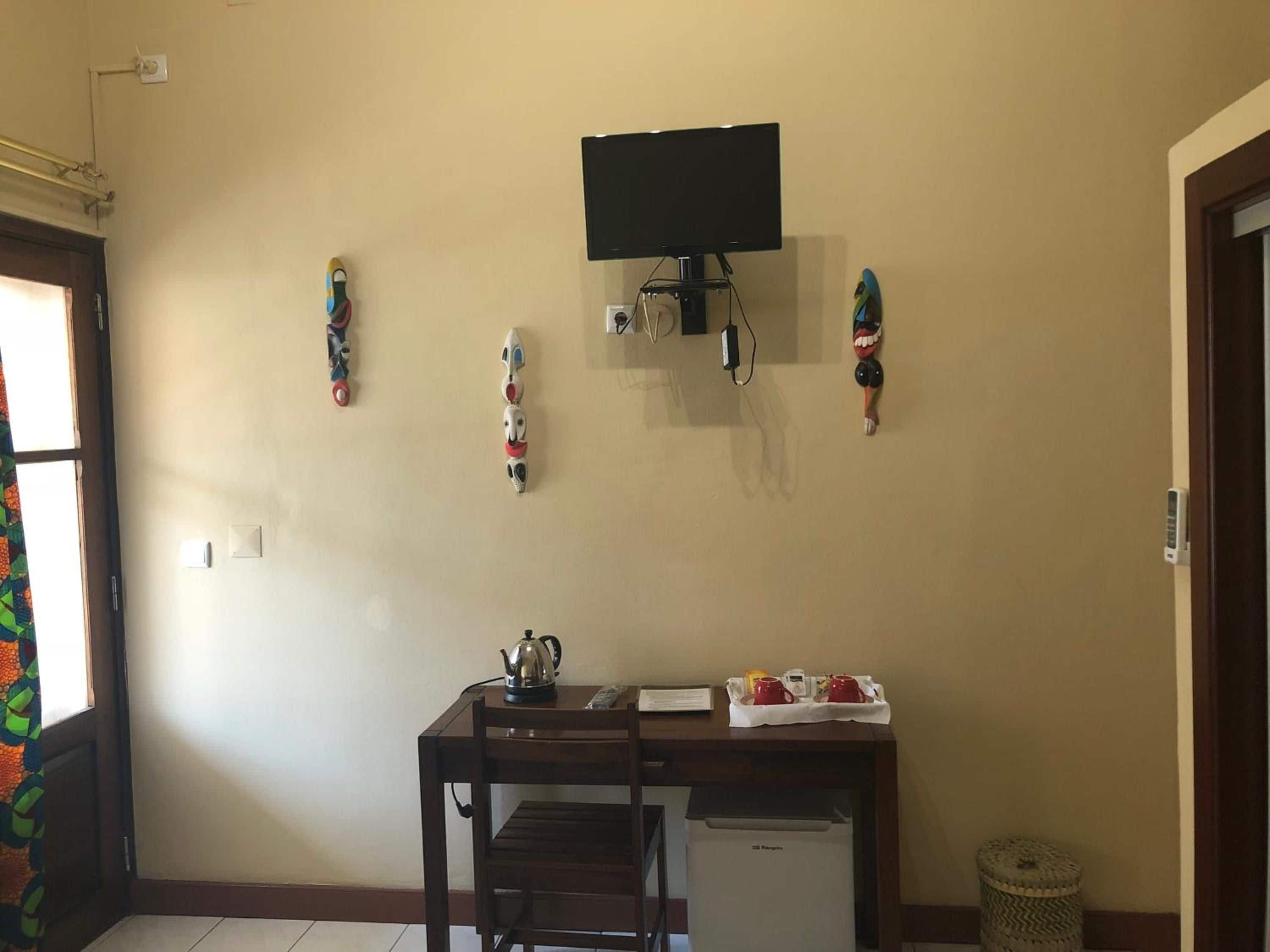 A room with a wooden desk, a television mounted on the wall, and decorative wall hangings.