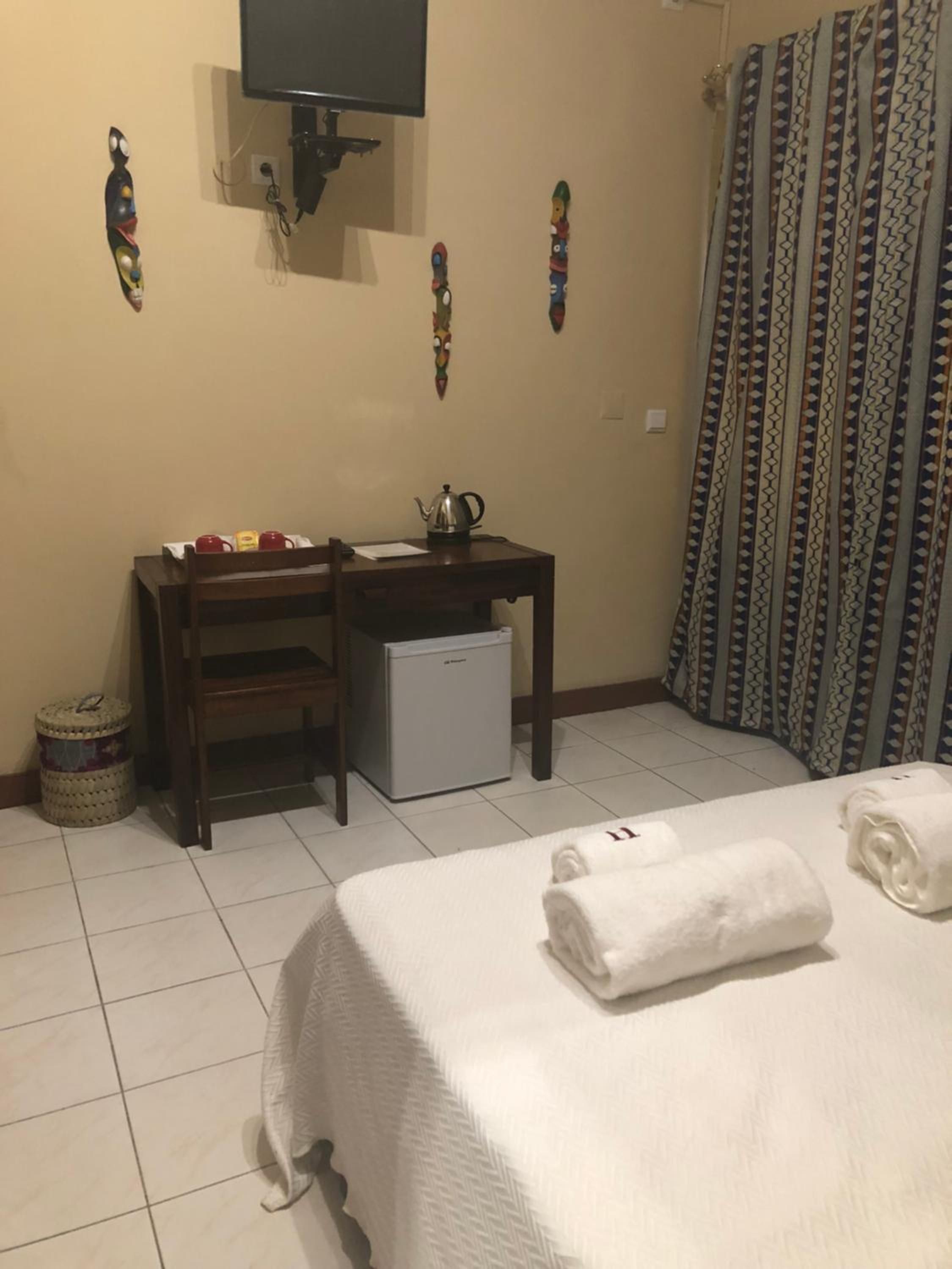 A hotel room with a bed, a desk with a computer, a small fridge, and a television on the wall.