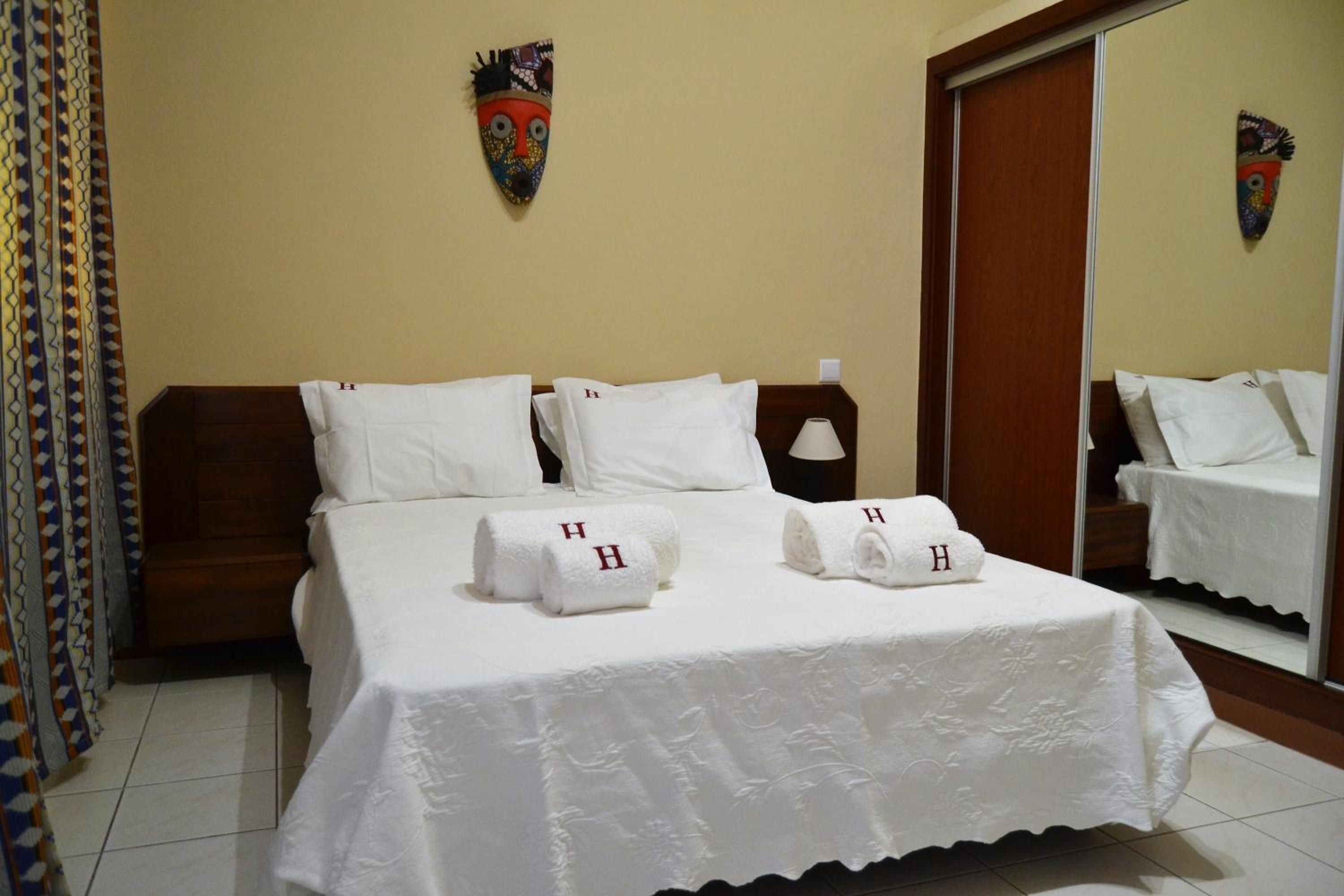A hotel room with a bed, pillows, a nightstand, a mirror, and a curtain.