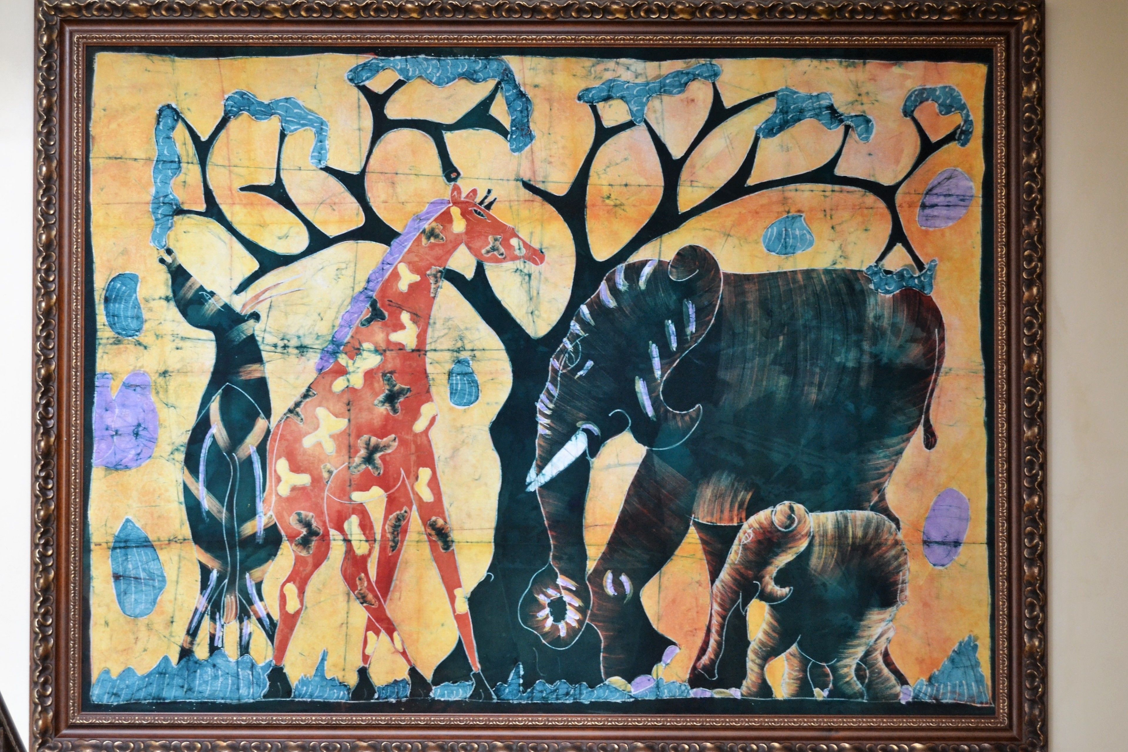 A framed artwork depicting a giraffe, elephant, and rhinoceros under a tree.