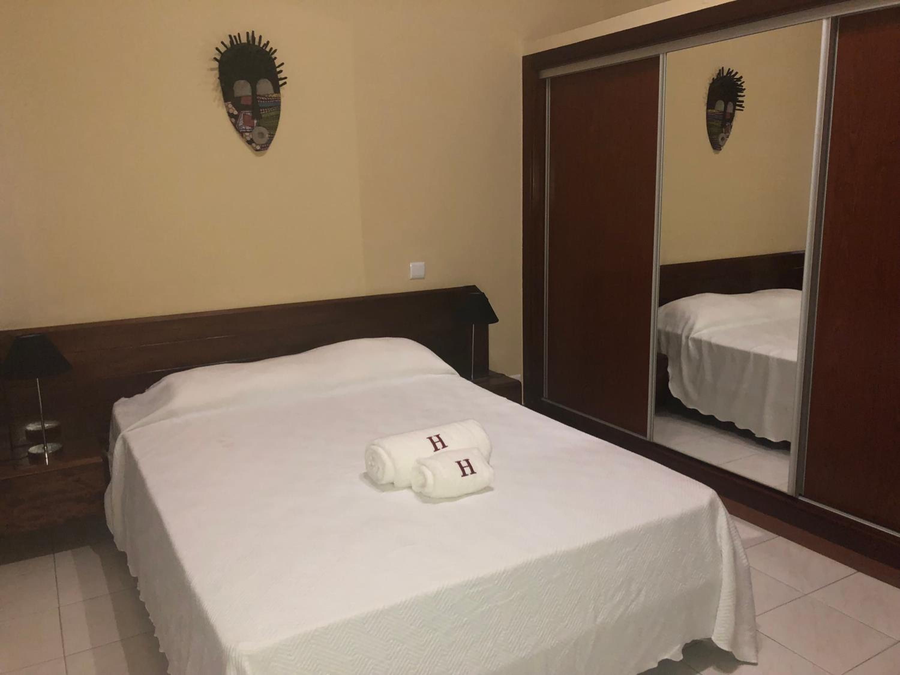Habitación de hotel con cama, mesita de noche, lámpara y armario con espejo.