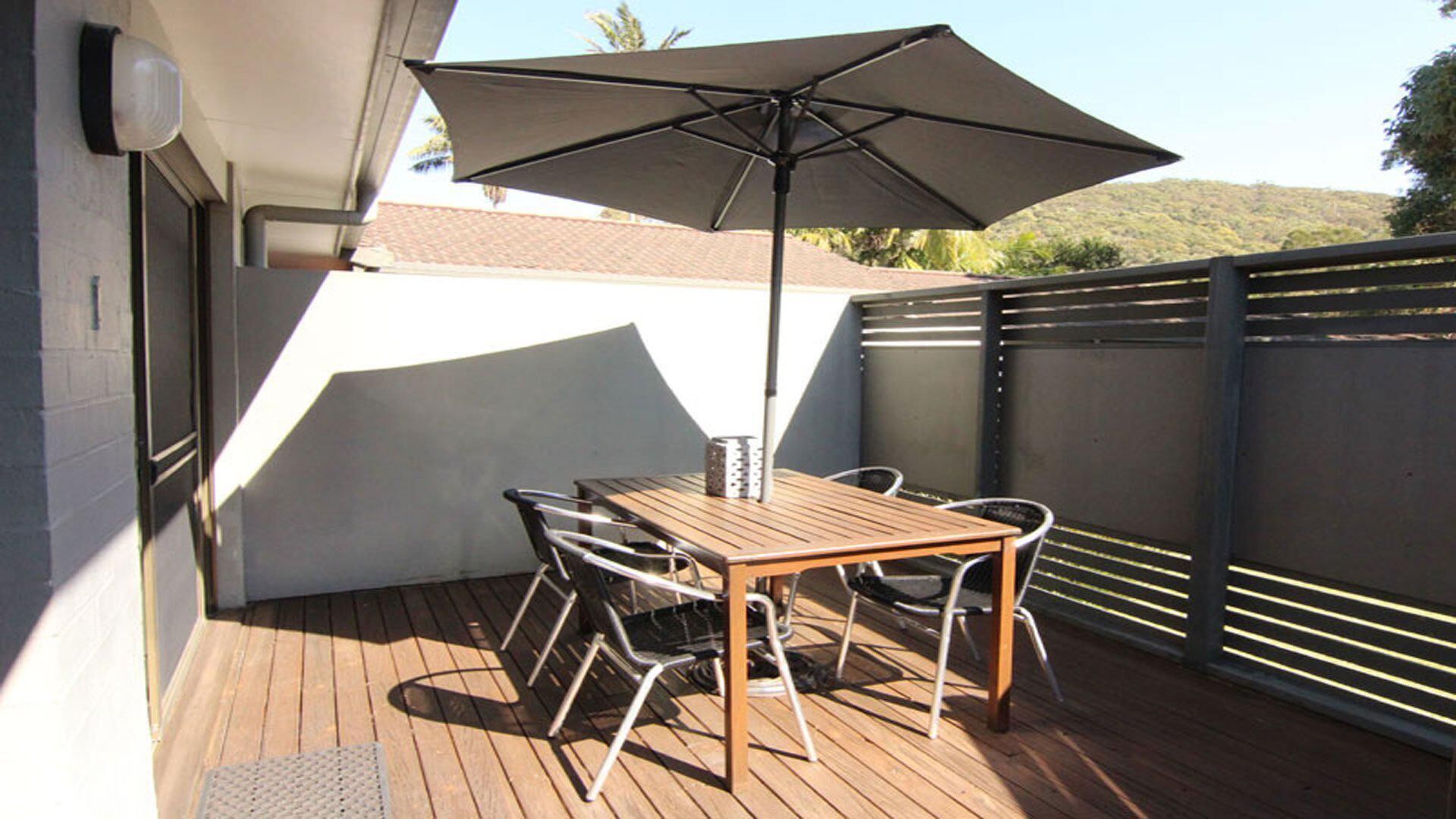 Una terraza de madera con una mesa, sillas, una sombrilla y una valla de metal.