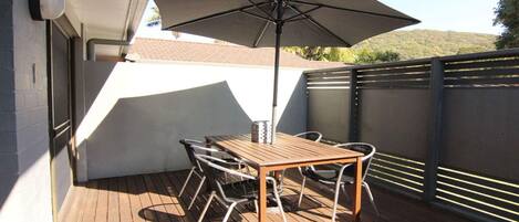 Una terraza de madera con una mesa, sillas, una sombrilla y una valla de metal.
