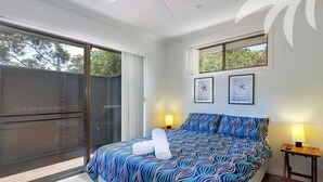 A bedroom with a large bed, two bedside lamps, a sliding glass door, and two wall clocks. - Aqua Apartment #1 - Pacific Palms Holidays (Blueys Beach)