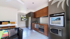 A modern kitchen with a built-in microwave, a dishwasher, and a large flat-screen TV. - Aqua Apartment #1 - Pacific Palms Holidays (Blueys Beach)