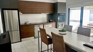 A modern kitchen with stainless steel appliances, wooden cabinets, and a dining area with wicker chairs. - Aqua Apartment #1 - Pacific Palms Holidays (Blueys Beach)