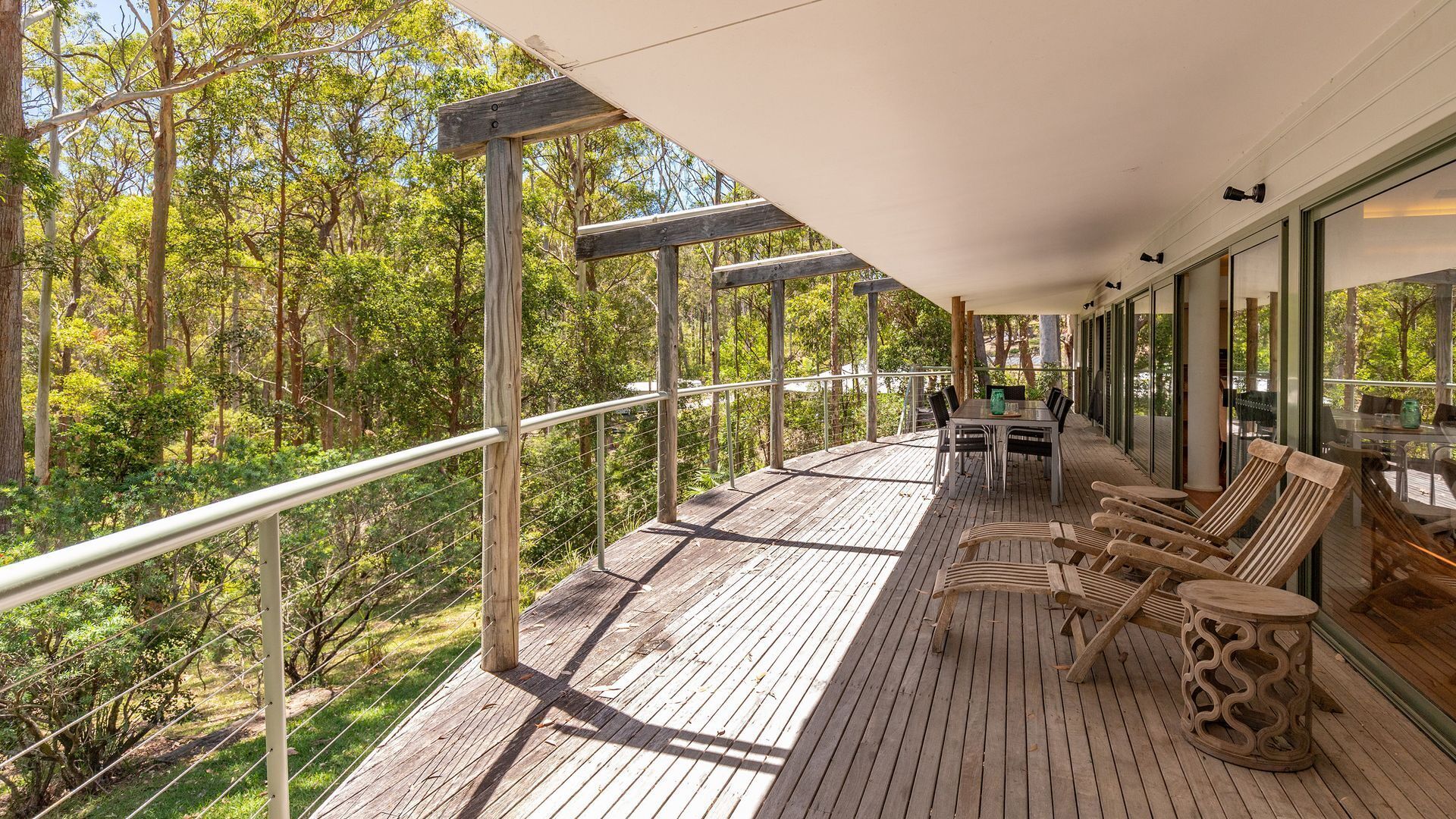Terraza de madera con mesa y sillas, con vistas a un área boscosa.
