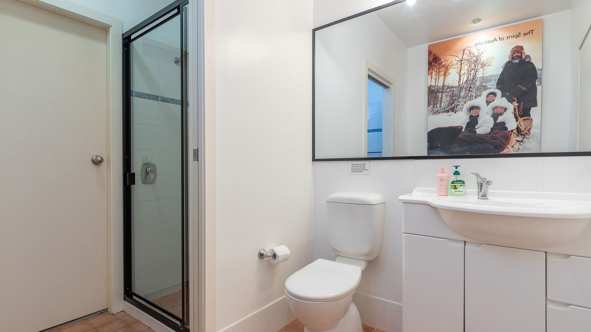 A bathroom with a glass shower door, a toilet, a sink, and a mirror.