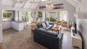 A spacious living area with a dark leather sofa, a dining table with chairs, and a kitchen area with white cabinets. - Twin Peaks 1 at Boomerang Beach (Boomerang Beach)