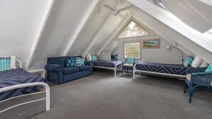 A triangular attic bedroom with a bed, two seating areas, and a window with a view. - Twin Peaks 1 at Boomerang Beach (Boomerang Beach)