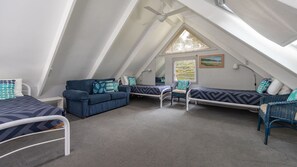 A triangular attic bedroom with a bed, two seating areas, and a window with a view. - Twin Peaks 1 at Boomerang Beach (Boomerang Beach)