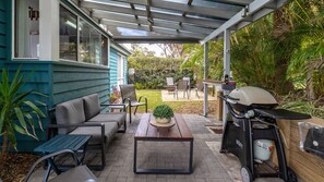 A covered patio with a grill, seating area, and a view of the backyard.