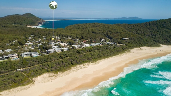 Vista aérea de una zona costera con playa, un bosque denso y una área residencial con casas.