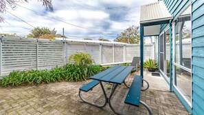 A patio with a picnic table, a white fence, and a building with blue siding. - Twin Peaks 1 at Boomerang Beach (Boomerang Beach)