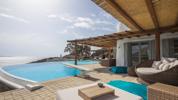 Zona de piscina con una pérgola de madera, mobiliario de mimbre y vistas al mar.