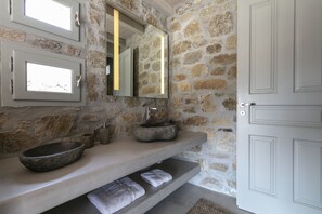 A bathroom with a stone wall, a large mirror, a stone sink, and a white door.