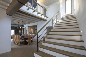 A staircase with wooden steps and metal railings, leading to a second-floor area with a dining table and chairs.