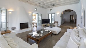 Amplia sala de estar con chimenea, sofás blancos, una mesa de centro y un televisor.