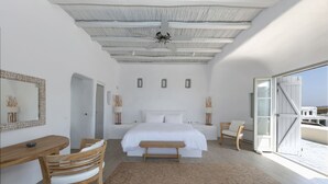 Un dormitorio con una cama grande, un banco de madera, un escritorio y una silla. Hay una ventana grande con vistas al exterior.