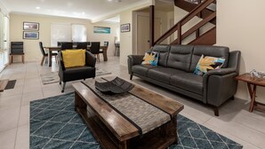 Ein Wohnzimmer mit einer Couch, einem Couchtisch und einer Bank. Im Hintergrund ist eine Treppe zu sehen.