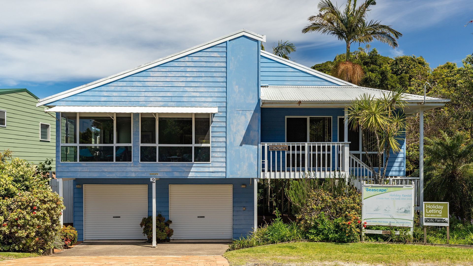A two-story building with a blue exterior, a balcony, and a sign indicating it's a holiday rental.