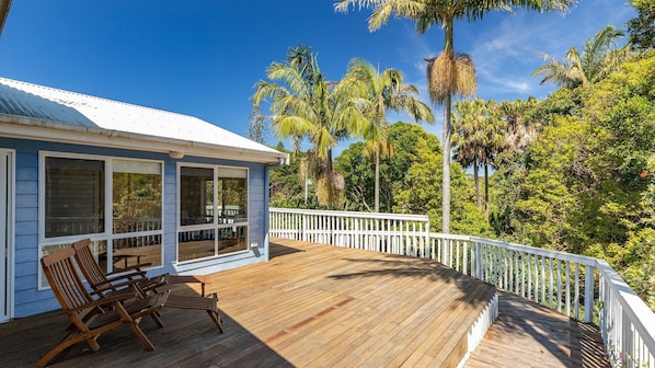 A wooden deck with a railing, overlooking a tropical landscape with palm trees.