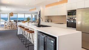 A modern kitchen with a large island, bar stools, a dishwasher, and a view of the ocean. - Ningaloo - Boomerang Beach (Boomerang Beach)