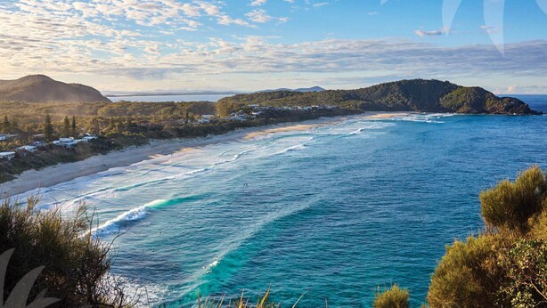 A coastal landscape with a beach, ocean, and hills in the background. - Oceanside 17  -  Breezes (Boomerang Beach)