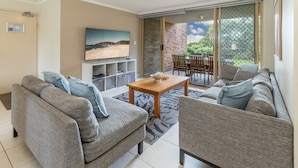 A living room with a sofa set, a coffee table, and a TV mounted on the wall. - Oceanside 17  -  Breezes (Boomerang Beach)