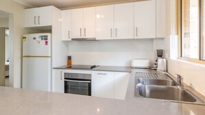 A modern kitchen with white cabinets, a built-in oven, a toaster, and a stainless steel sink. - Oceanside 17  -  Breezes (Boomerang Beach)
