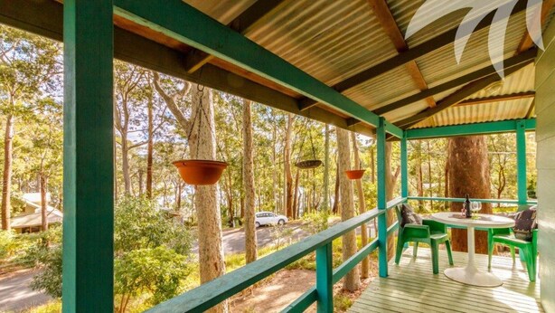 A covered outdoor area with a wooden deck, green railings, and hanging planters. - Fyshwicks Cottage - Pacific Palms Holidays (Smiths Lake)