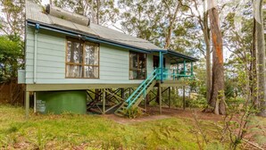 A two-story house with a balcony and stairs, surrounded by trees. - Fyshwicks Cottage - Pacific Palms Holidays (Smiths Lake)