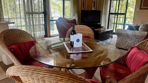 A living room with wicker furniture, a glass table, and a television. - Fyshwicks Cottage - Pacific Palms Holidays (Smiths Lake)