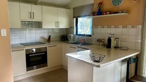A compact kitchen with white cabinets, a built-in oven, a sink, and a window. - Fyshwicks Cottage - Pacific Palms Holidays (Smiths Lake)