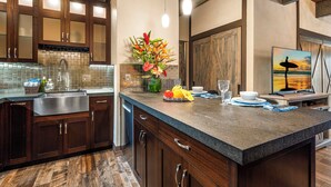 A modern kitchen with dark wood cabinets, a granite countertop, and a backsplash of small tiles. - Loft Style Completely Remodeled Condo (Kailua-Kona)