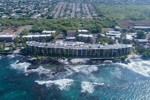 Un hôtel en bord de mer, avec plusieurs étages, entouré par les vagues de l’océan et adossé à un quartier résidentiel.