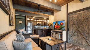 A cozy living area with a sofa, a coffee table, and a dining table. There is a kitchen in the background with a large wooden door. - Loft Style Completely Remodeled Condo (Kailua-Kona)
