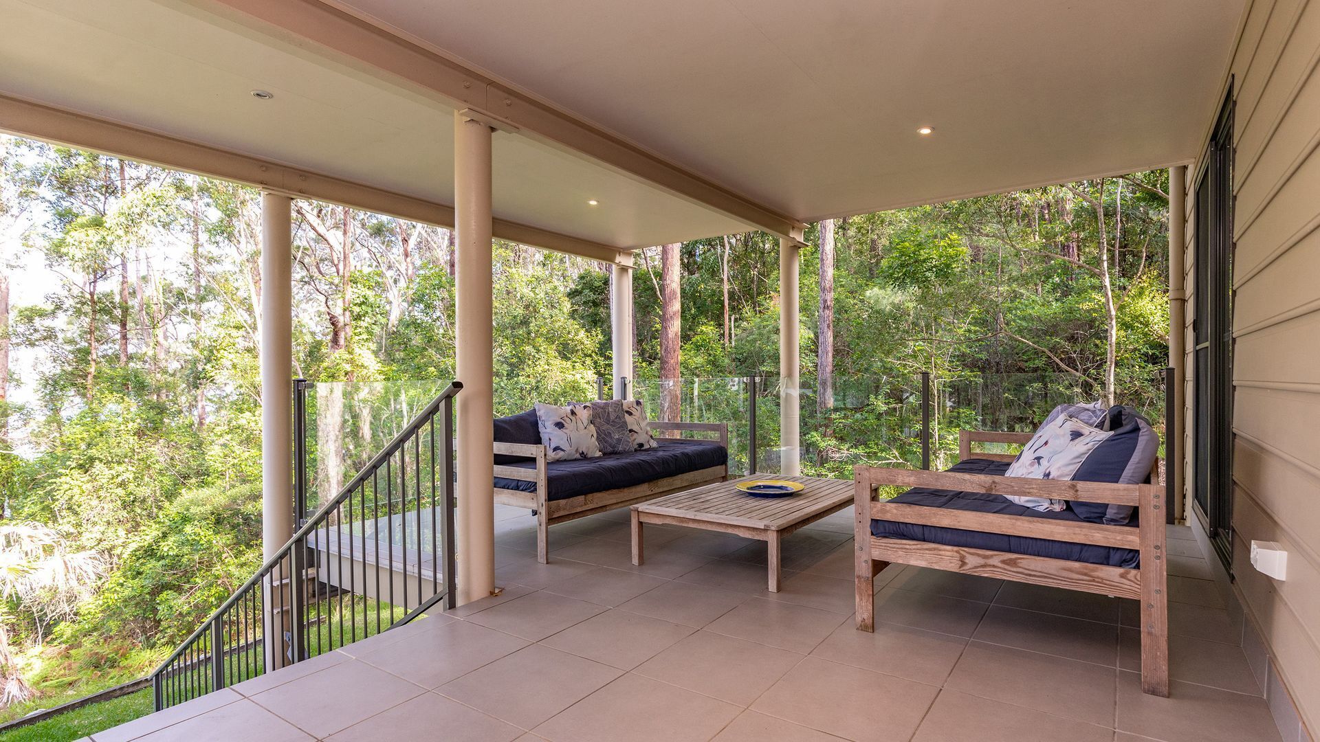 A covered outdoor seating area with two sofas and a coffee table, surrounded by trees.