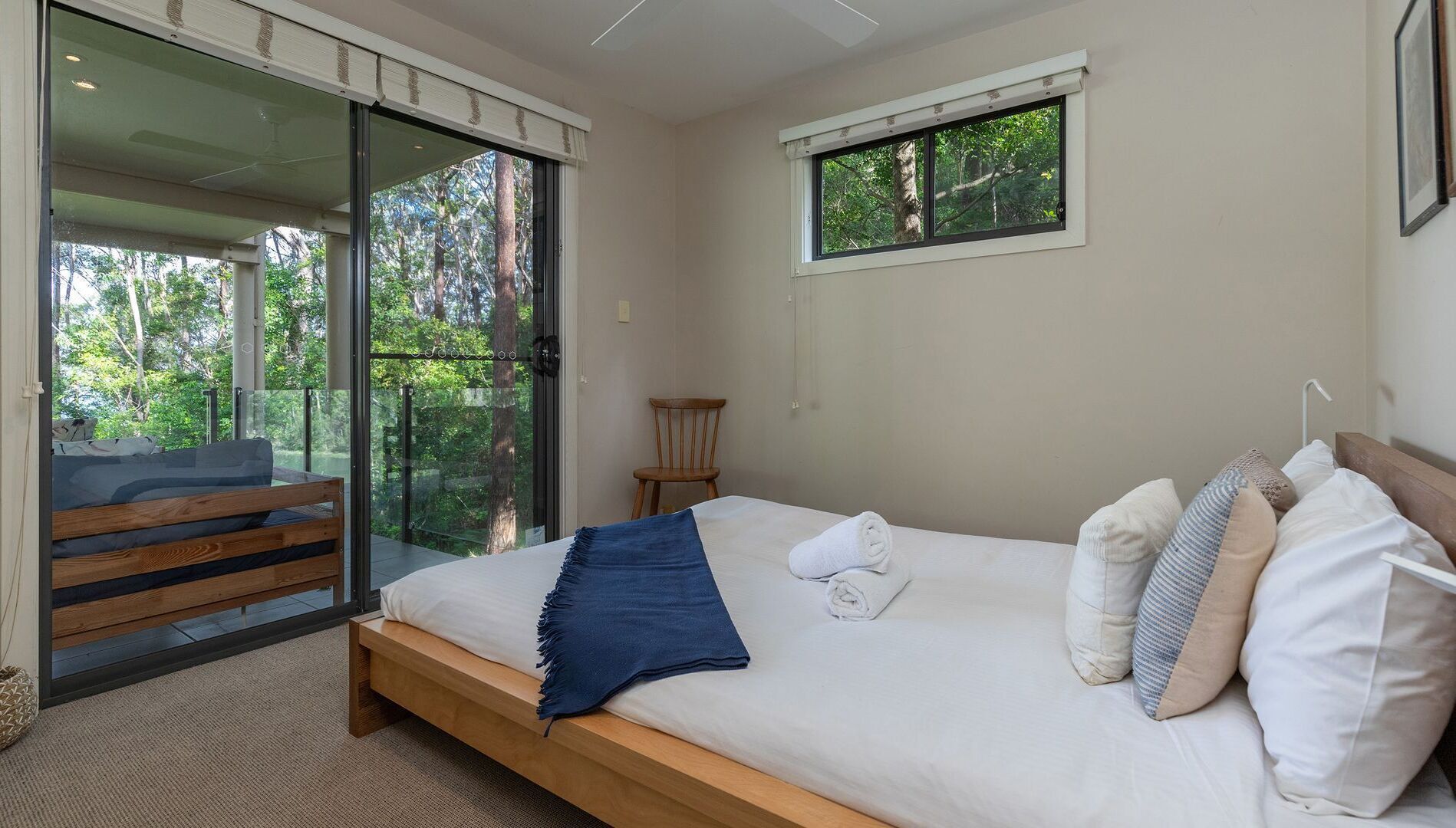 Ein Schlafzimmer mit einem großen Bett, einer hölzernen Bank, einem Sessel und einem Balkon mit Glastüren.