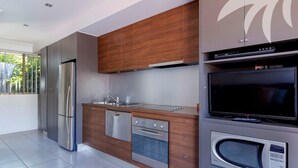 A modern kitchen with stainless steel appliances, a built-in oven, microwave, and a flat-screen TV. - Aqua Apartment #3 - Pacific Palms Holidays (Blueys Beach)