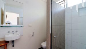A bathroom with a white sink, a mirror, and a shower area with tiled walls. - Aqua Apartment #3 - Pacific Palms Holidays (Blueys Beach)