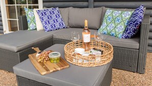 A wicker sofa with patterned cushions, a wooden serving tray with grapes and a jar, and a bottle of wine on a matching ottoman. - Large villa on private vineyard in prime and secluded location (Pokolbin)