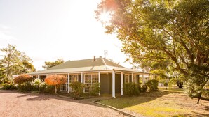 A single-story house with a covered porch, surrounded by a gravel driveway and various shrubs and trees. - Large villa on private vineyard in prime and secluded location (Pokolbin)