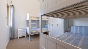 Habitación con literas, una mesita de noche pequeña y una ventana con cortinas.