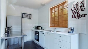 A modern kitchen with white cabinetry, a stainless steel sink, and a window with bamboo blinds. - Aqua Apartment #4 - Pacific Palms Holidays (Blueys Beach)