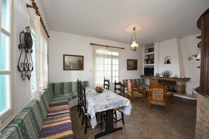A traditional living room with a sofa set, dining table, and chairs. There is a fireplace with decorative items and a bookshelf. - Giameiko Traditional House Kalymnos (Kalymnos)