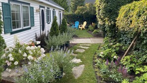 Ett vitt hus med gröna fönsterluckor, en trädgård med olika växter och blommor och två Adirondack-stolar.
