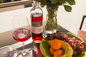 Une table avec une bouteille de vin, un verre de vin rouge, un vase de roses et un saladier de fruits.